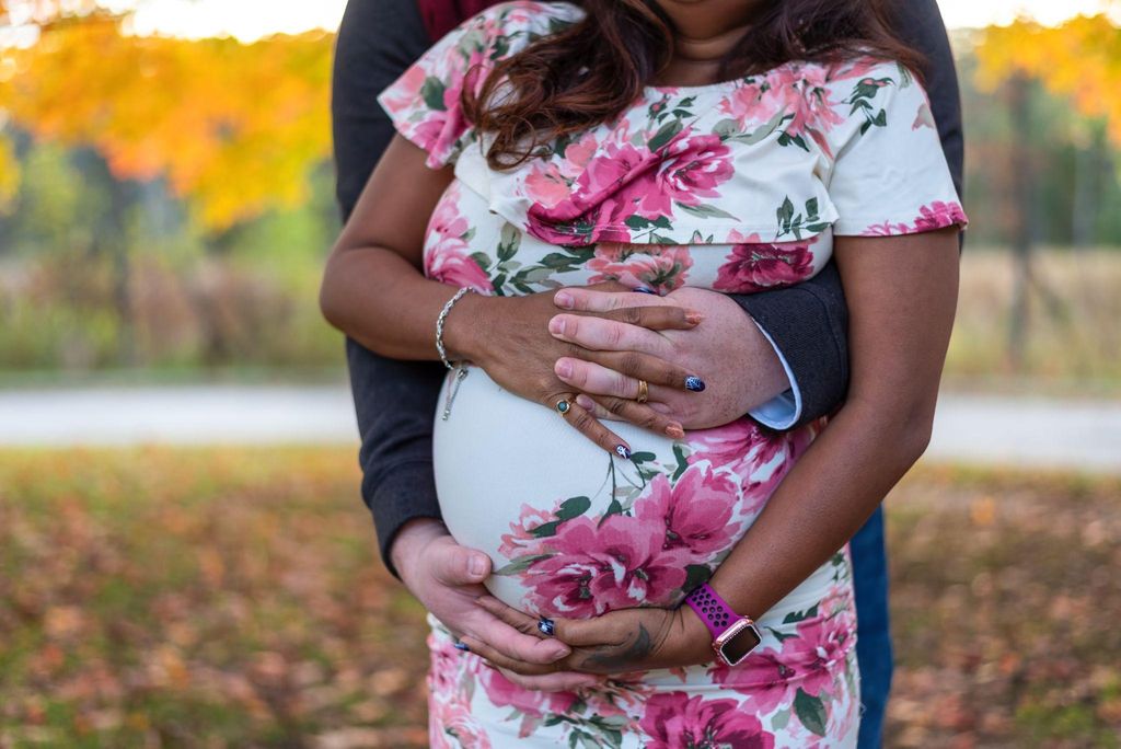 "A pregnant woman pondering her baby’s gender, with her partner’s armsaround her bump."