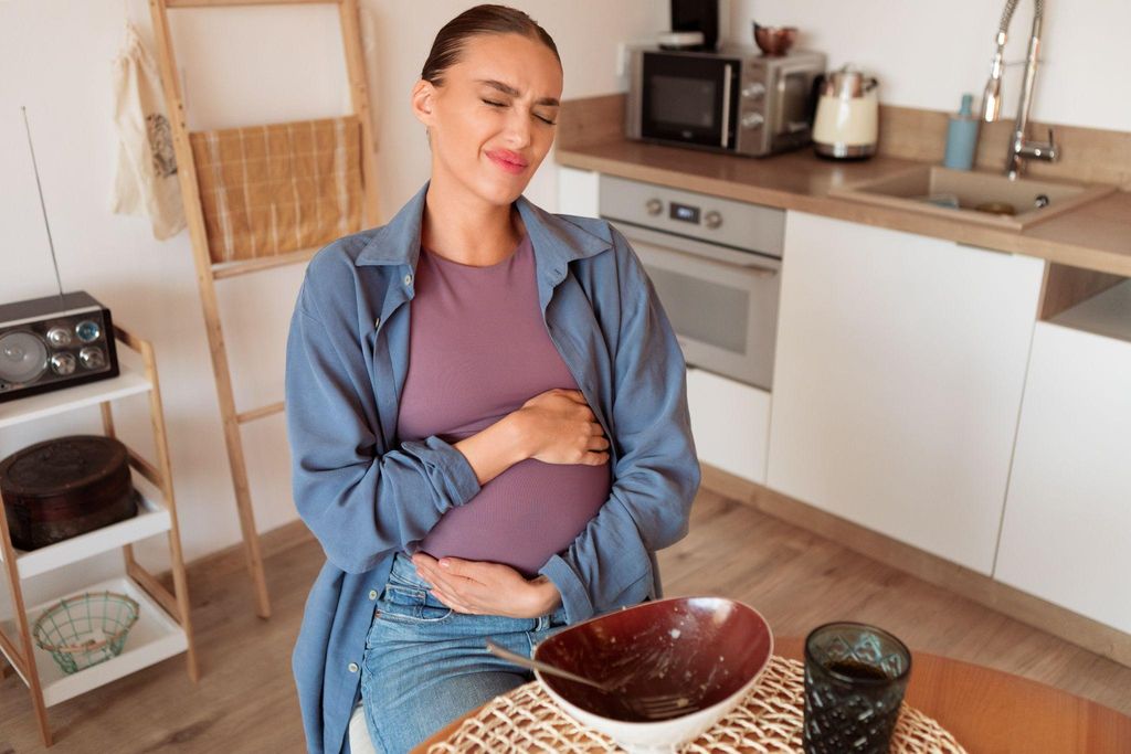 Pregnant woman with morning sickness holds tummy after eating.