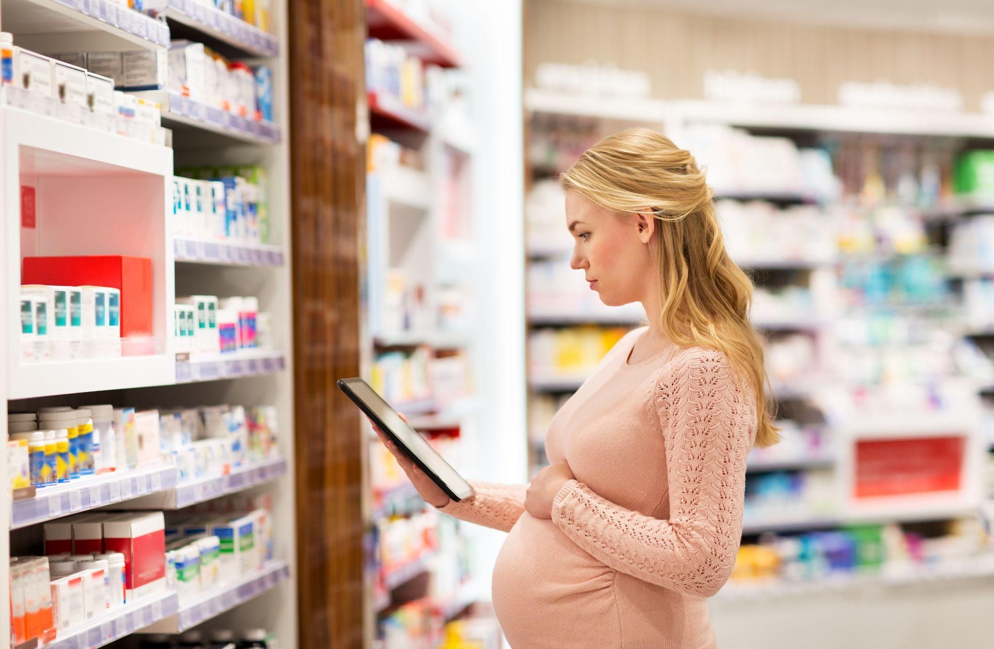 Pregnant woman researches the best antenal vitamins on iPad in pharmacy.