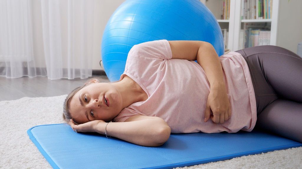 A pregnant woman lies on a yoga mat to manage antenatal pain.