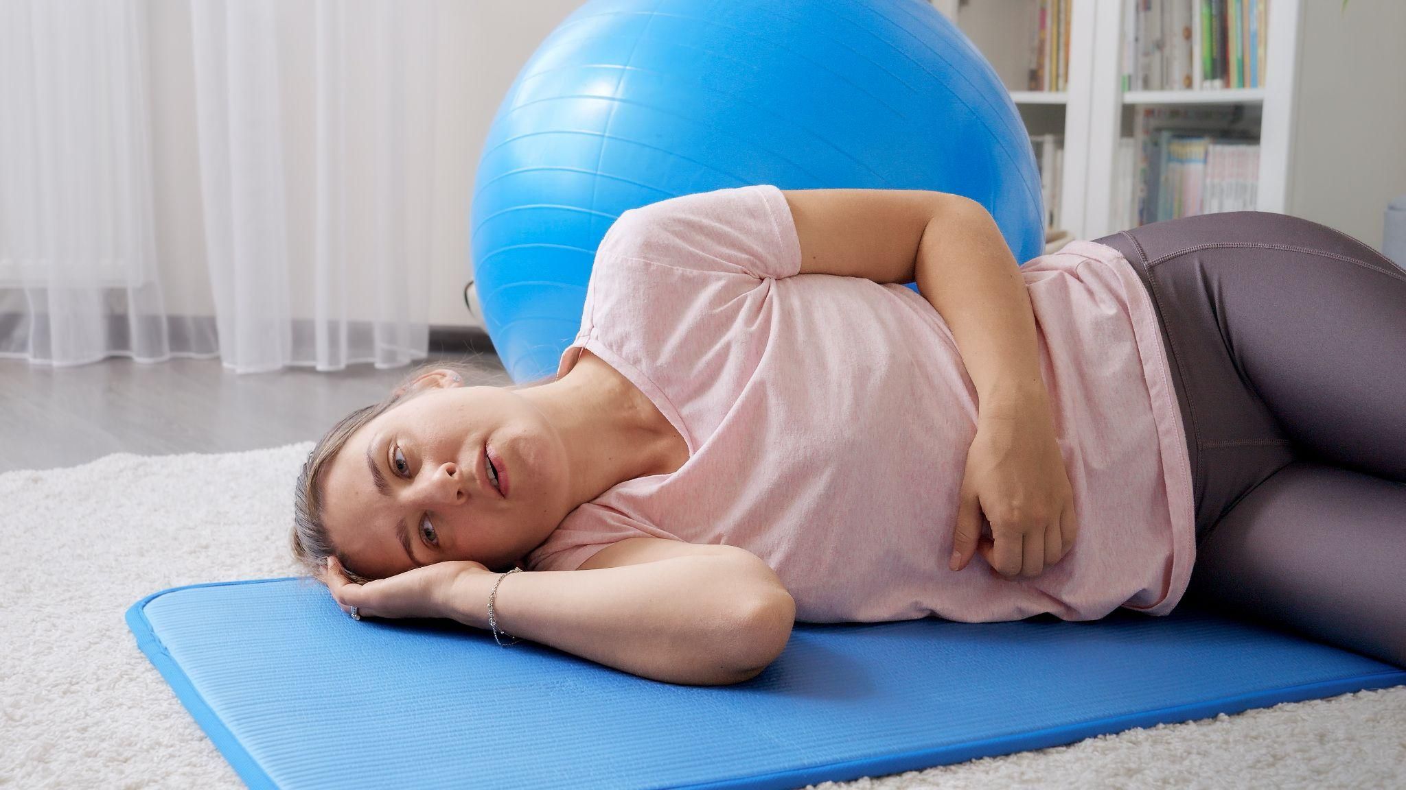 A pregnant woman lies on a yoga mat to manage antenatal pain.