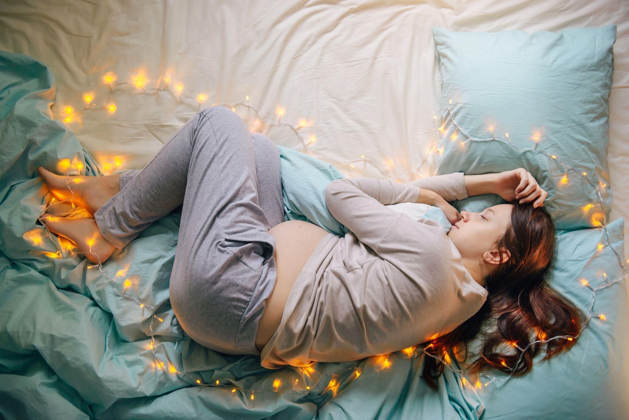 A pregnant woman sleeping on her side with a pregnancy pillow for support.