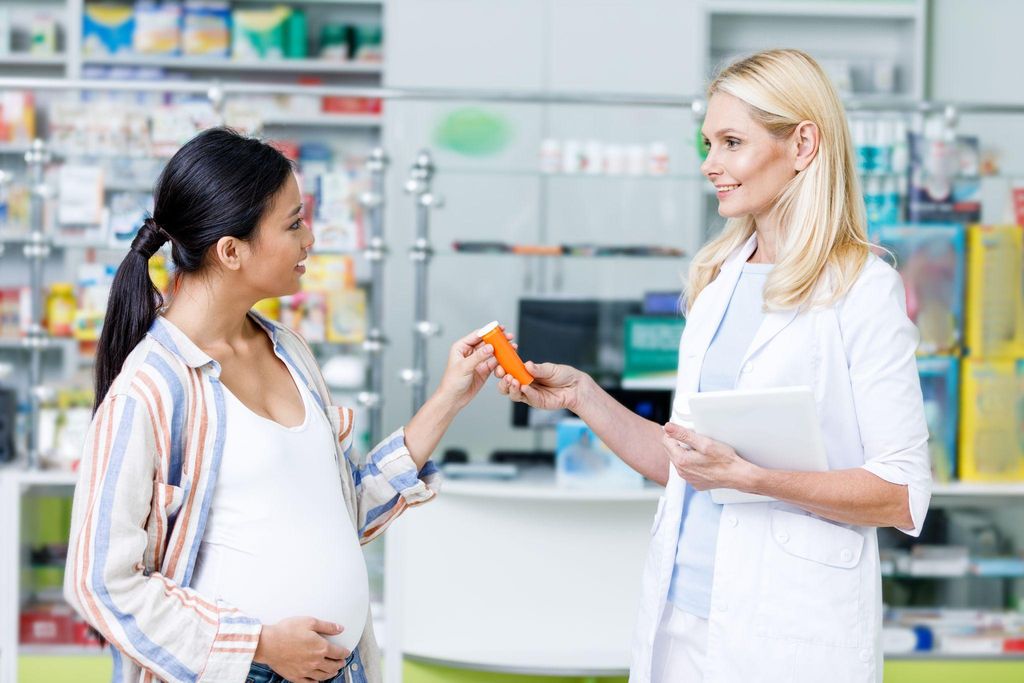 Expectant mother smiling as she receives free prescription medications at a UK pharmacy.