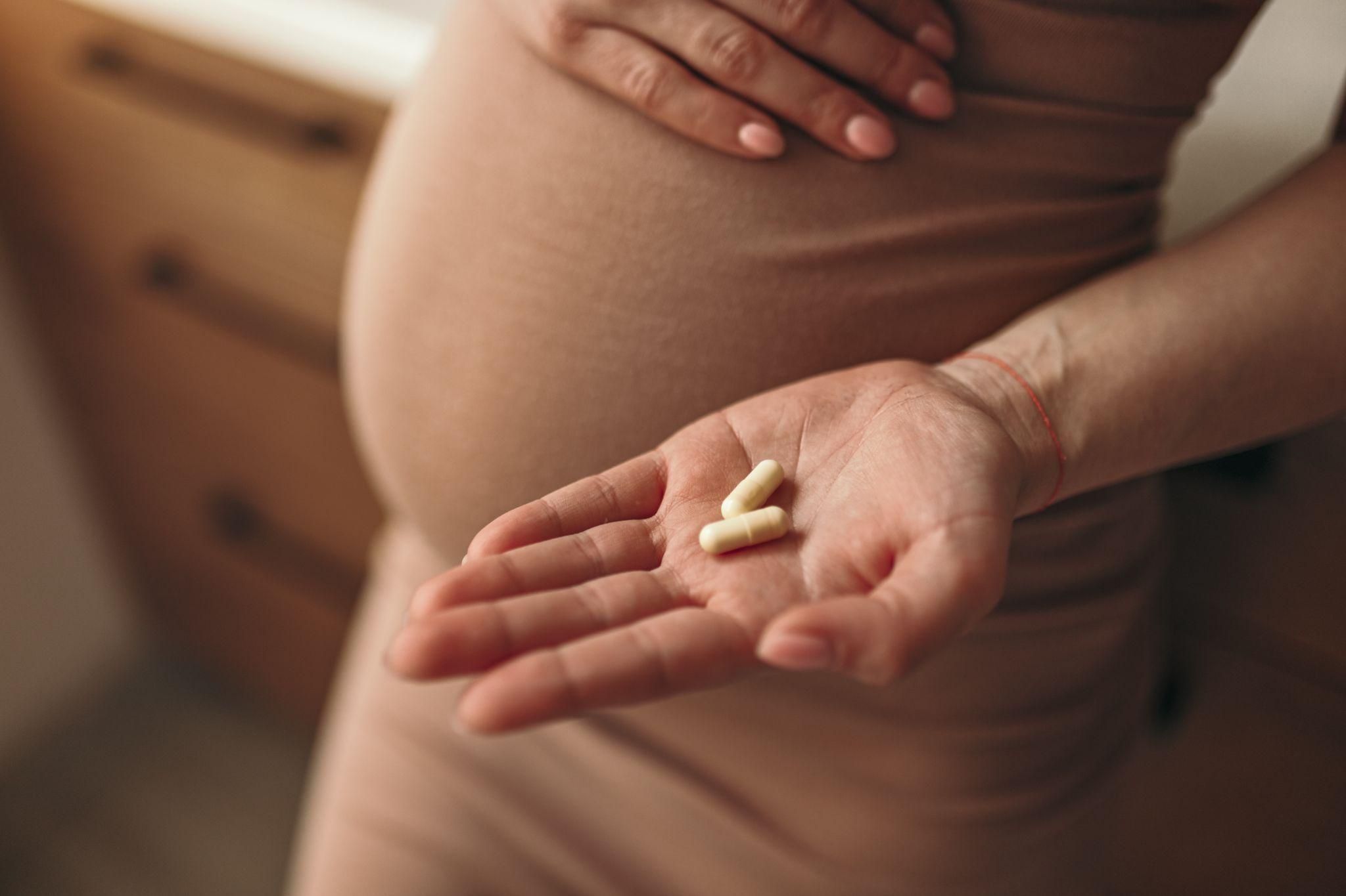 Pregnacare vitamins with a pregnant woman smiling in the background.