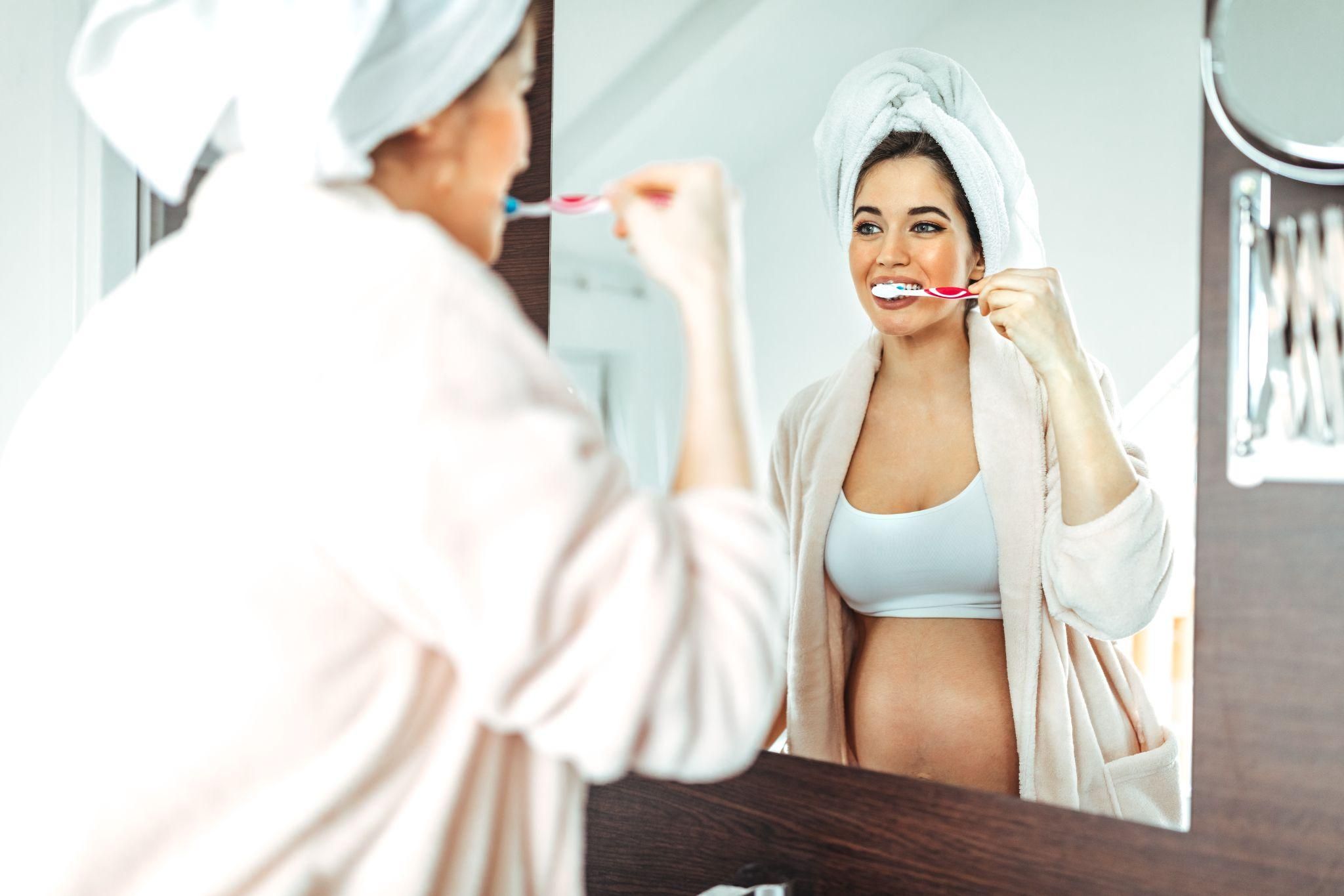 A pregnant woman brushing her teeth during pregnancy to maintain oral health.