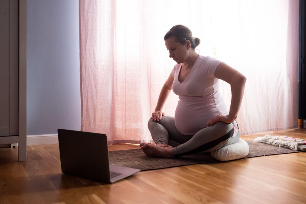 Pregnant woman watches online antenatal class on yoga mat at home.