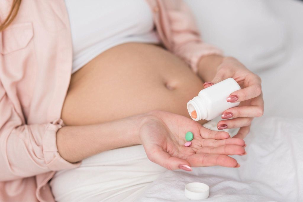 Pregnant woman empty vitamin pills onto hand.