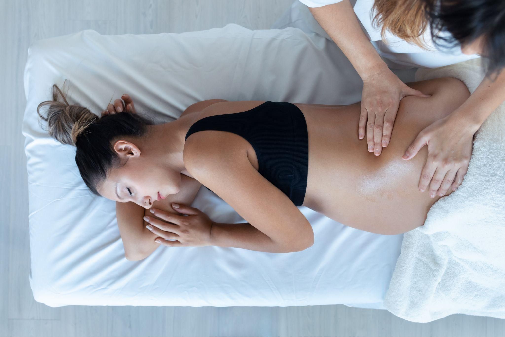 A pregnant woman enjoys an antenatal massage while lying on her side on a massage table.