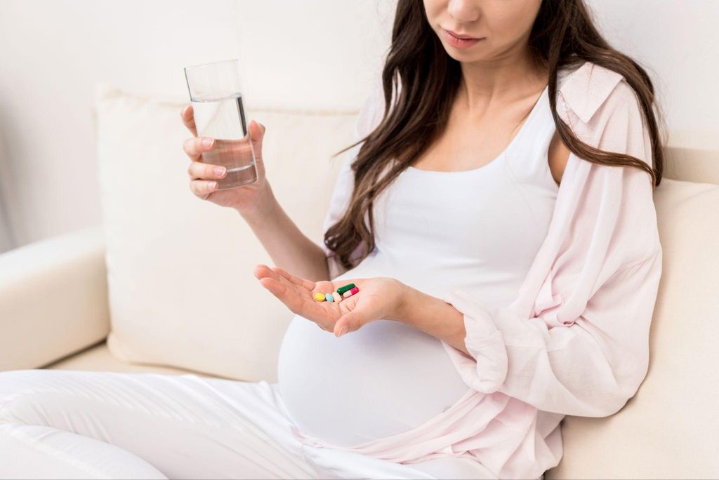 Pregnant woman takes handful of pills with a glass of water.