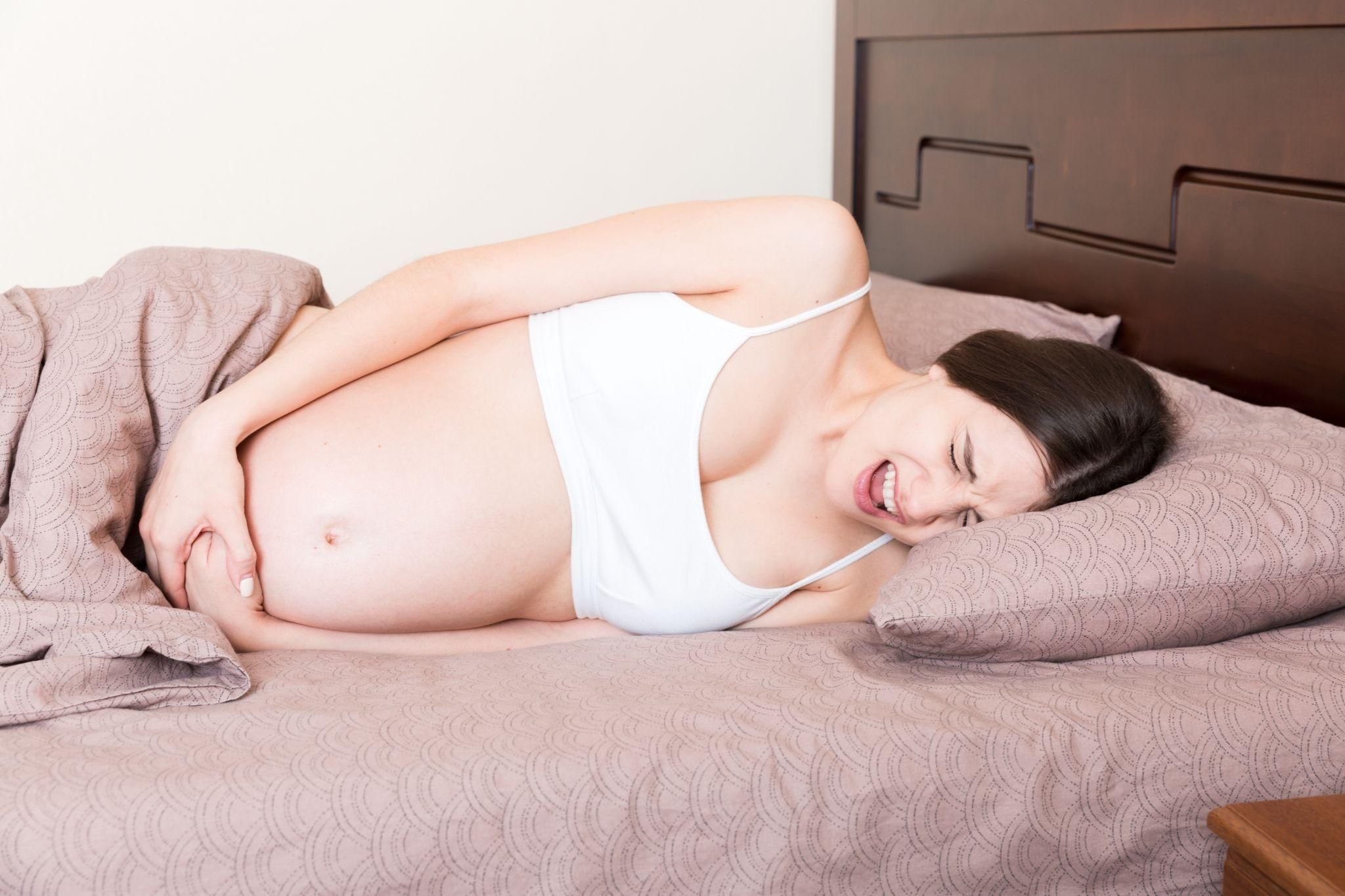 Pregnant woman lies on side, wincing with pelvic pain.