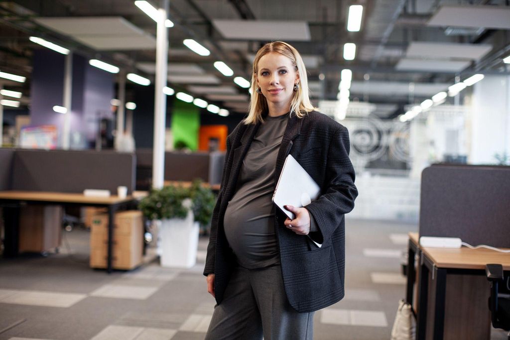 A pregnant woman sitting at her desk looking concerned about her job security while taking maternity leave.