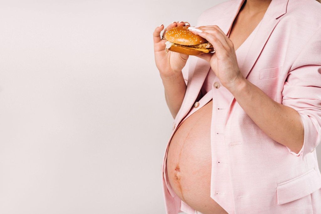 Pregnant woman eating hamburger with hands.