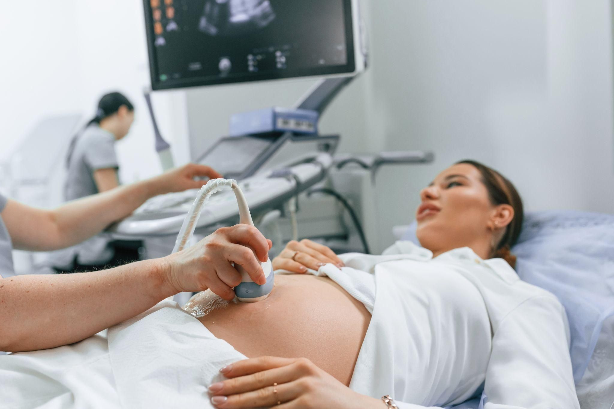 Pregnant woman has ultrasound scan with sonographer and radiologist during antenatal appointment.