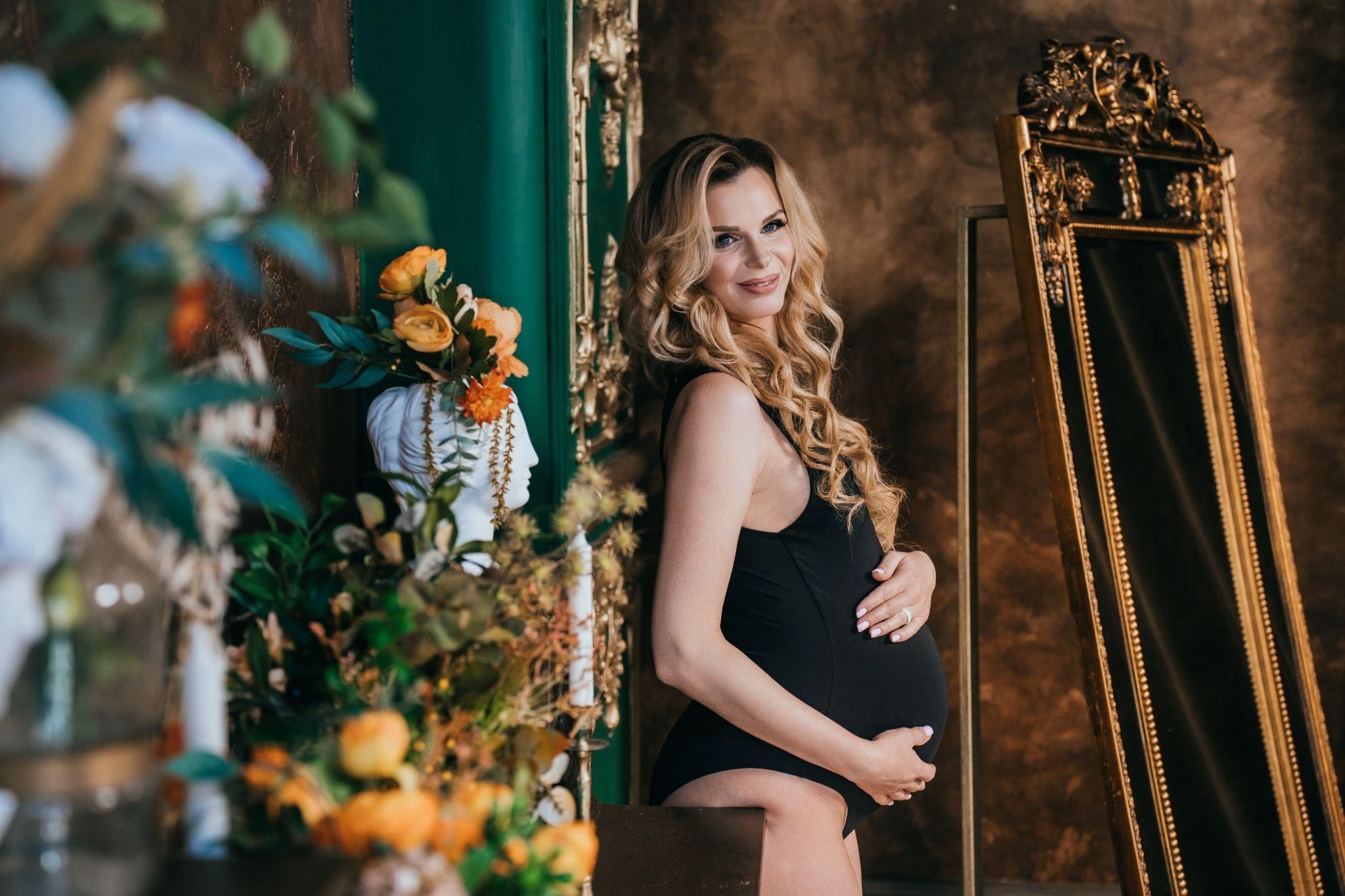 Pregnant woman applying sunscreen to her face outdoors.