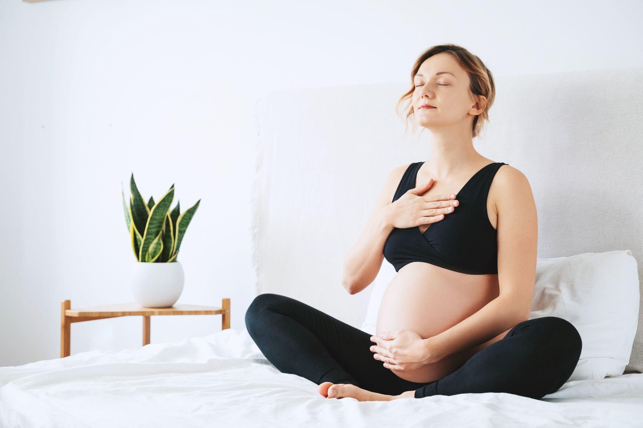 A pregnant woman sitting cross-legged, focused on her breathing to manage stress.