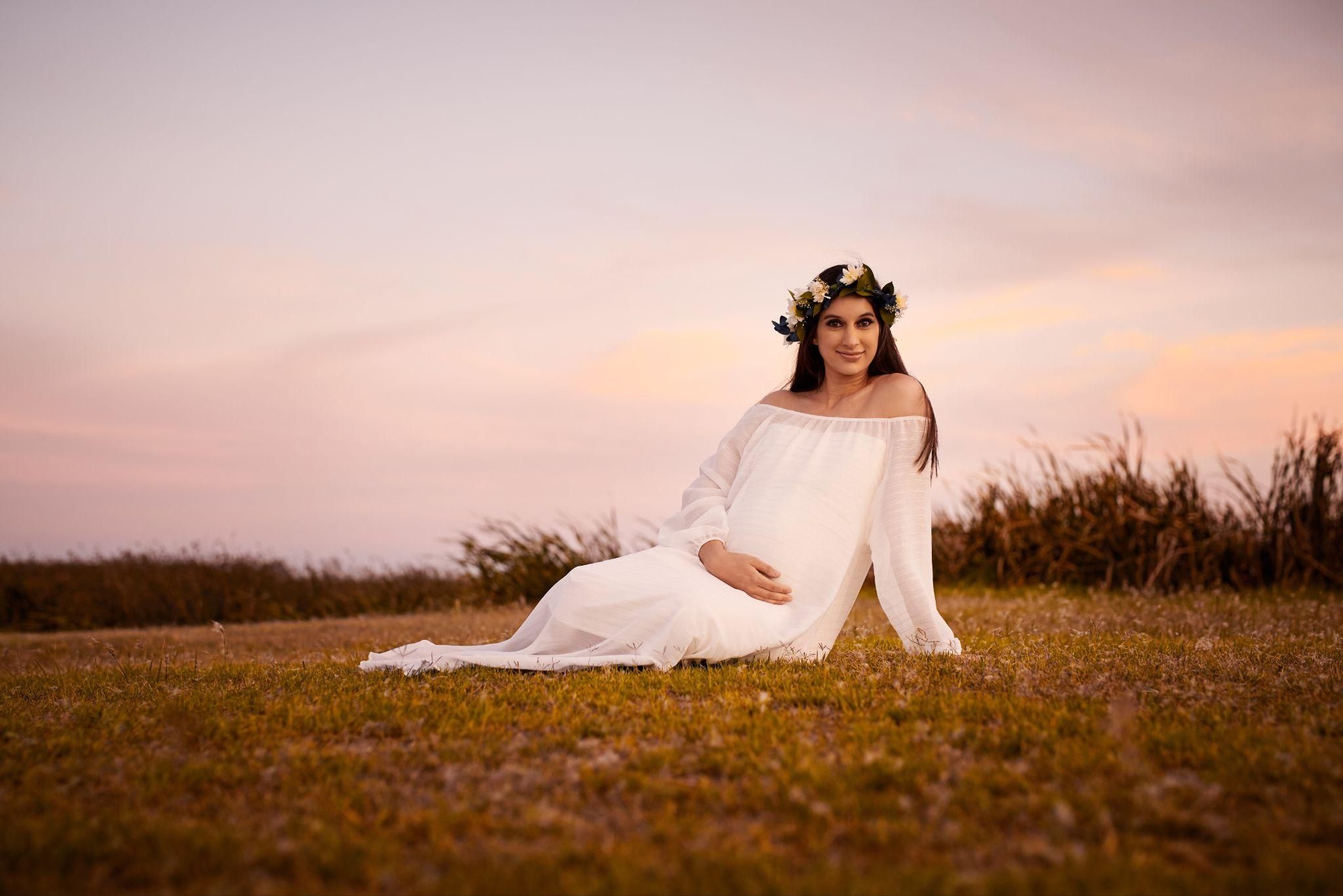 Pregnant woman in a studio photoshoot with a soft glow and neutral tones.