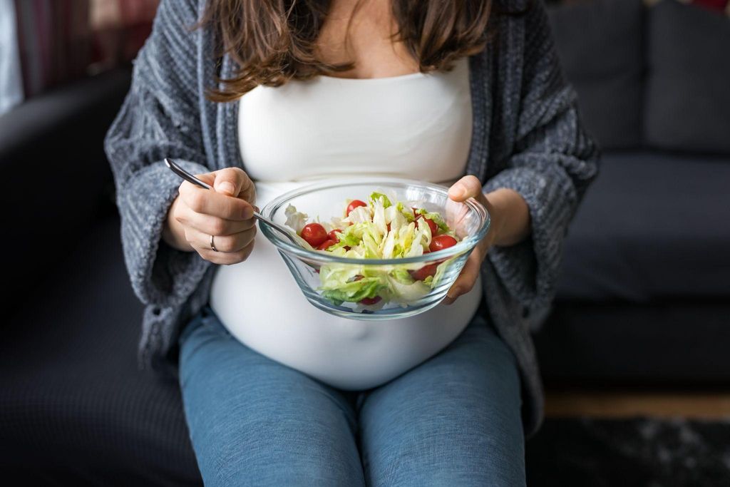 A smiling pregnant woman enjoying a nutritious meal during her antenatal journey.