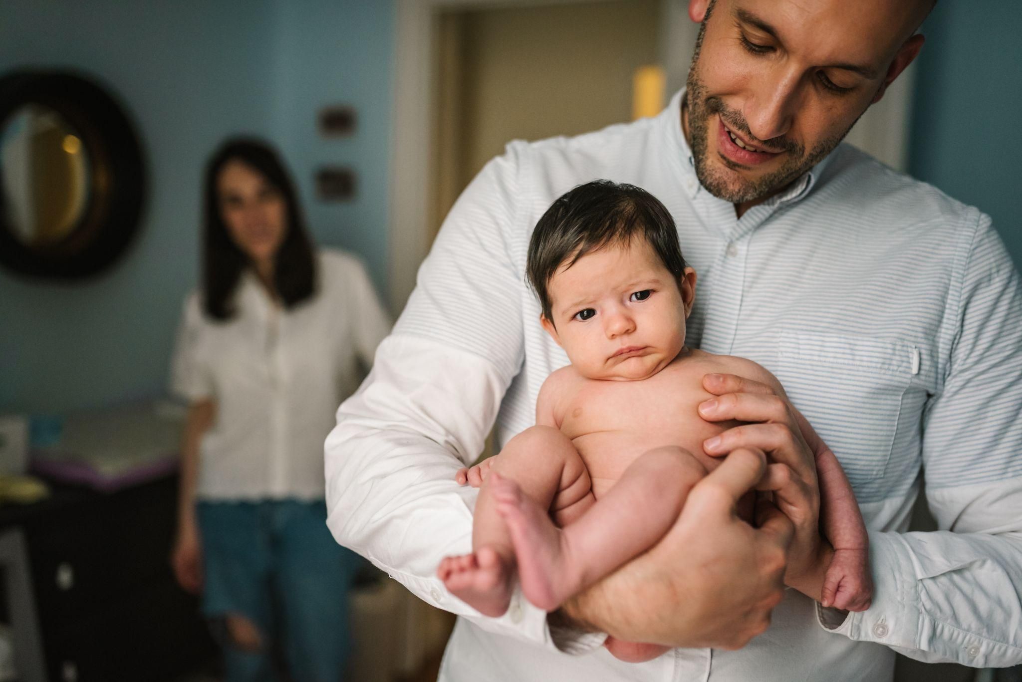 Father holding cute baby with mother in background.