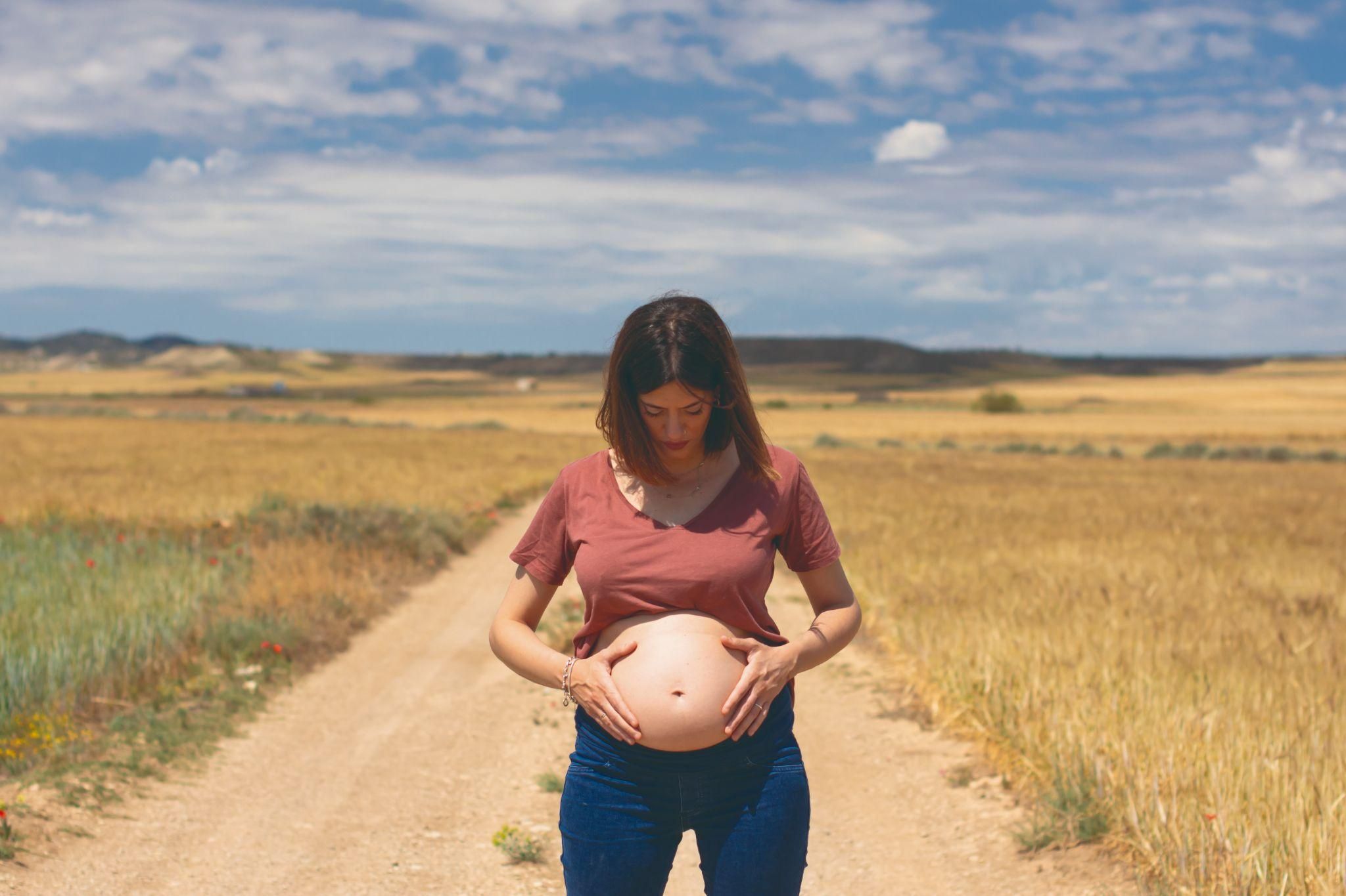 A serene pregnancy photoshoot with a mother-to-be standing in a field during golden hour.