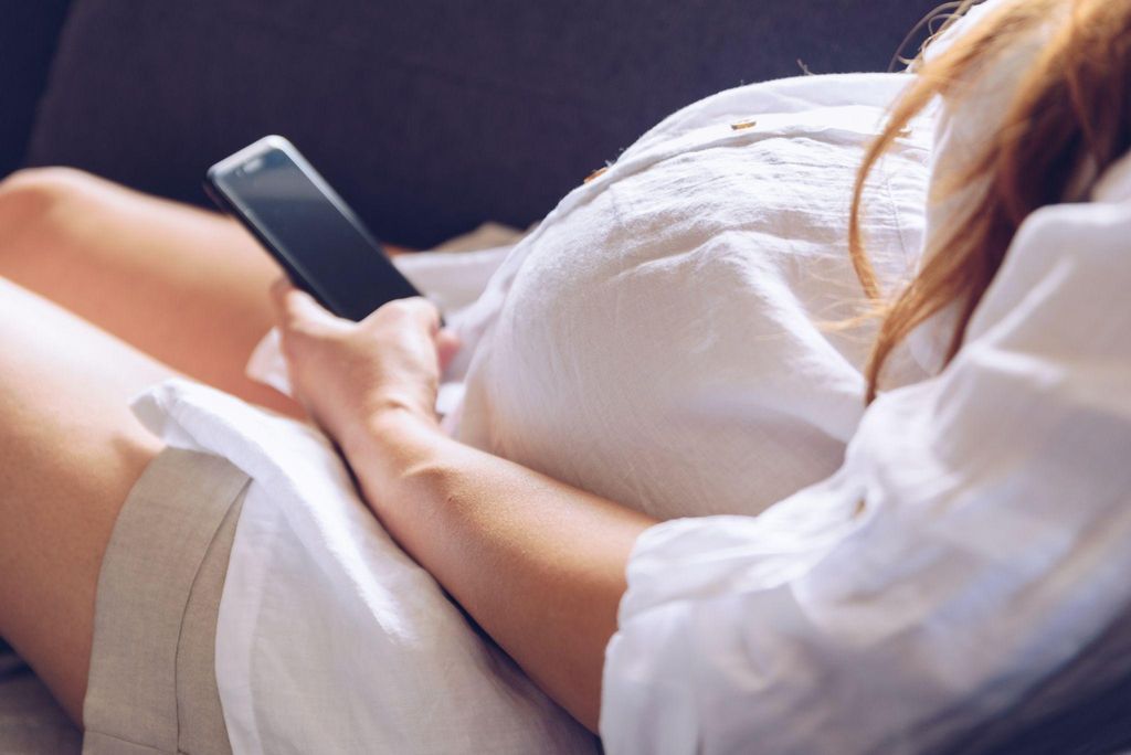 A woman using a pregnancy app on her phone, with baby development tracking displayed on the screen.