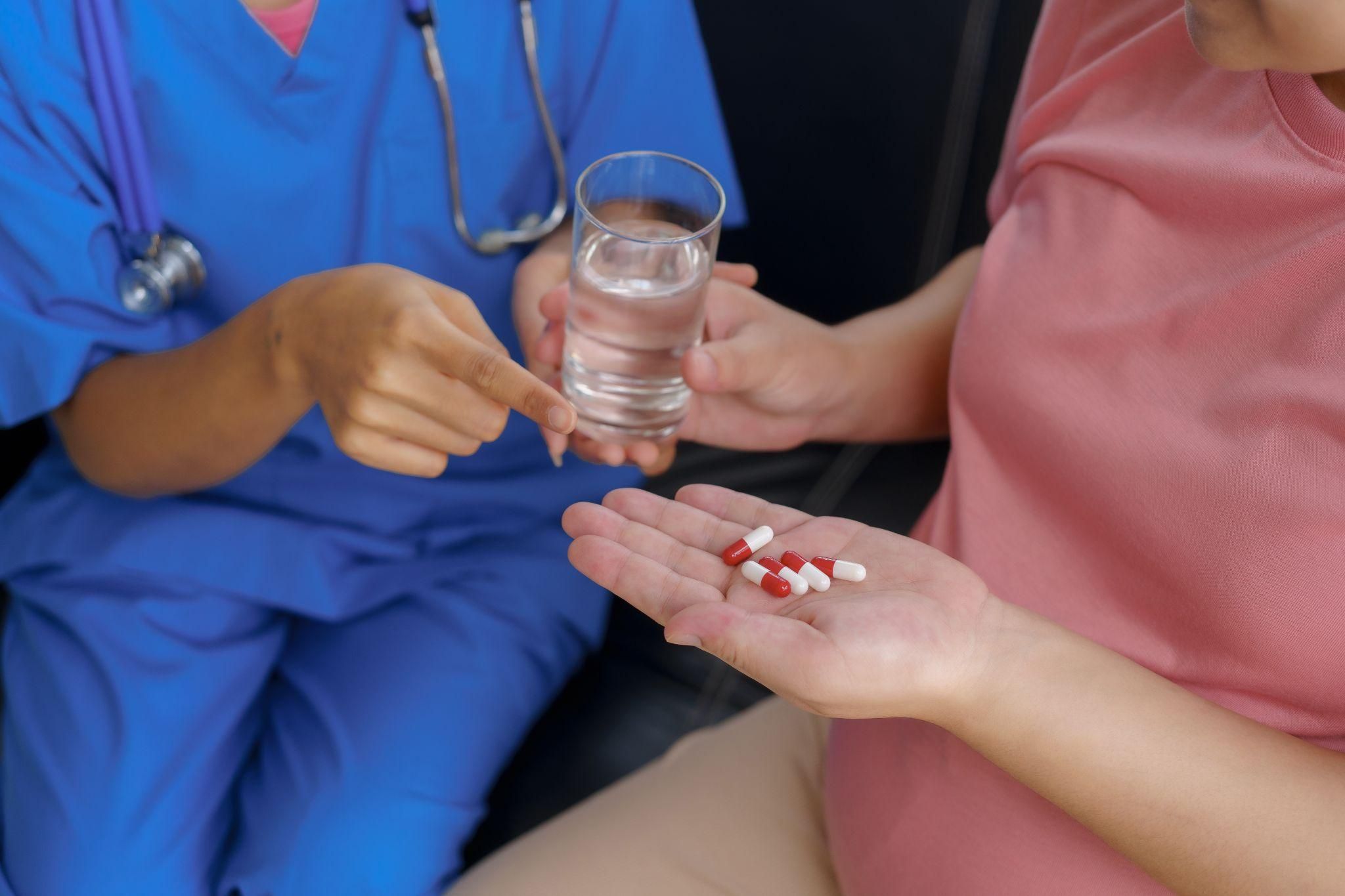 Midwife speaks to pregnant woman about medication and gives her a glass of water.