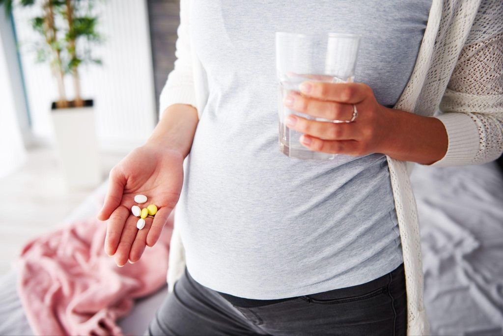 Pregnant woman takes five antenatal vitamins in the morning with a glass of water.