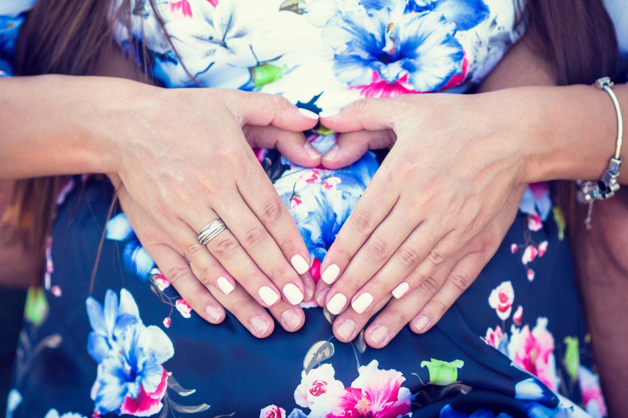 Pregnant couple with hands on baby bump in heart shape.