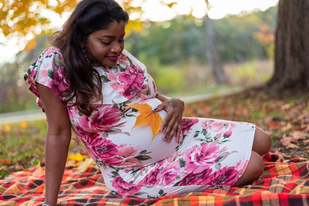 Pregant woman sits in a park on a picnic blanket under a tree. Antenatal anxiety coping measure.