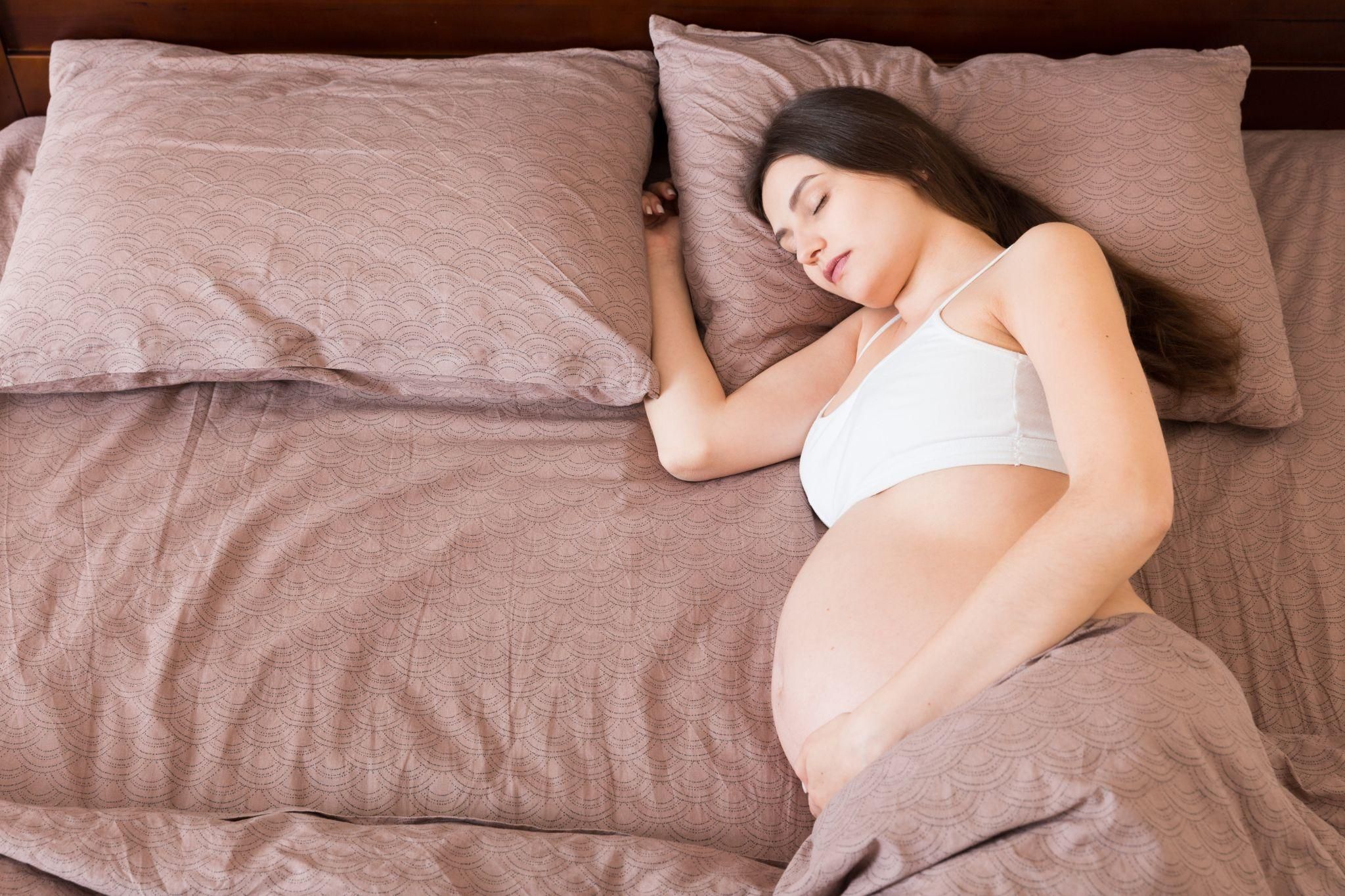 A pregnant woman resting in bed with a pillow for support.