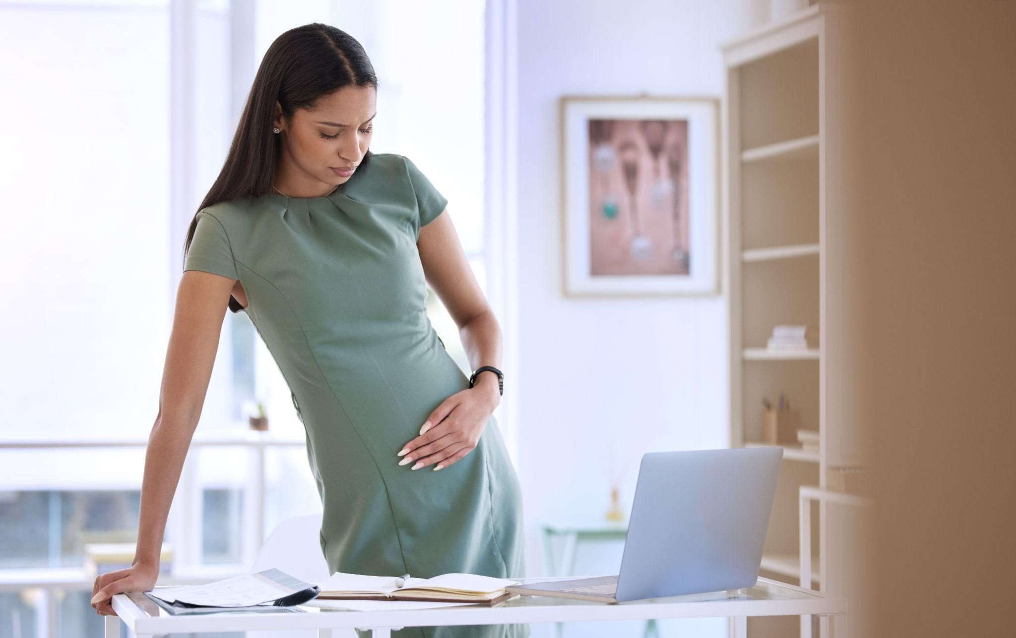 A pregnant woman managing her body heat at work using a fan and staying hydrated.