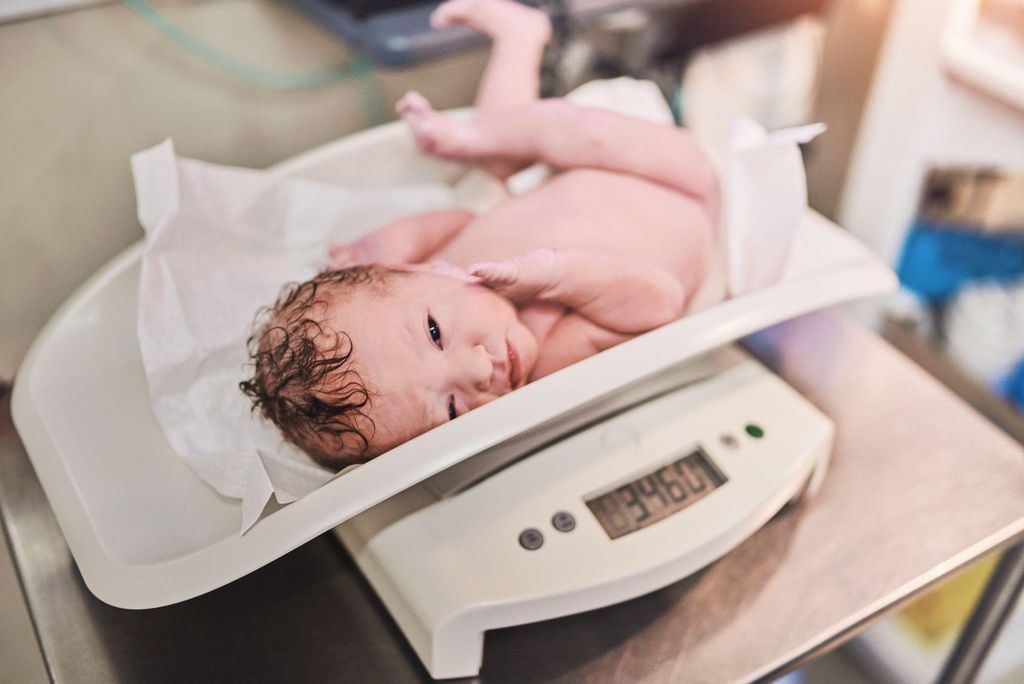 Female newborn weighed on scale after birth in hospital.