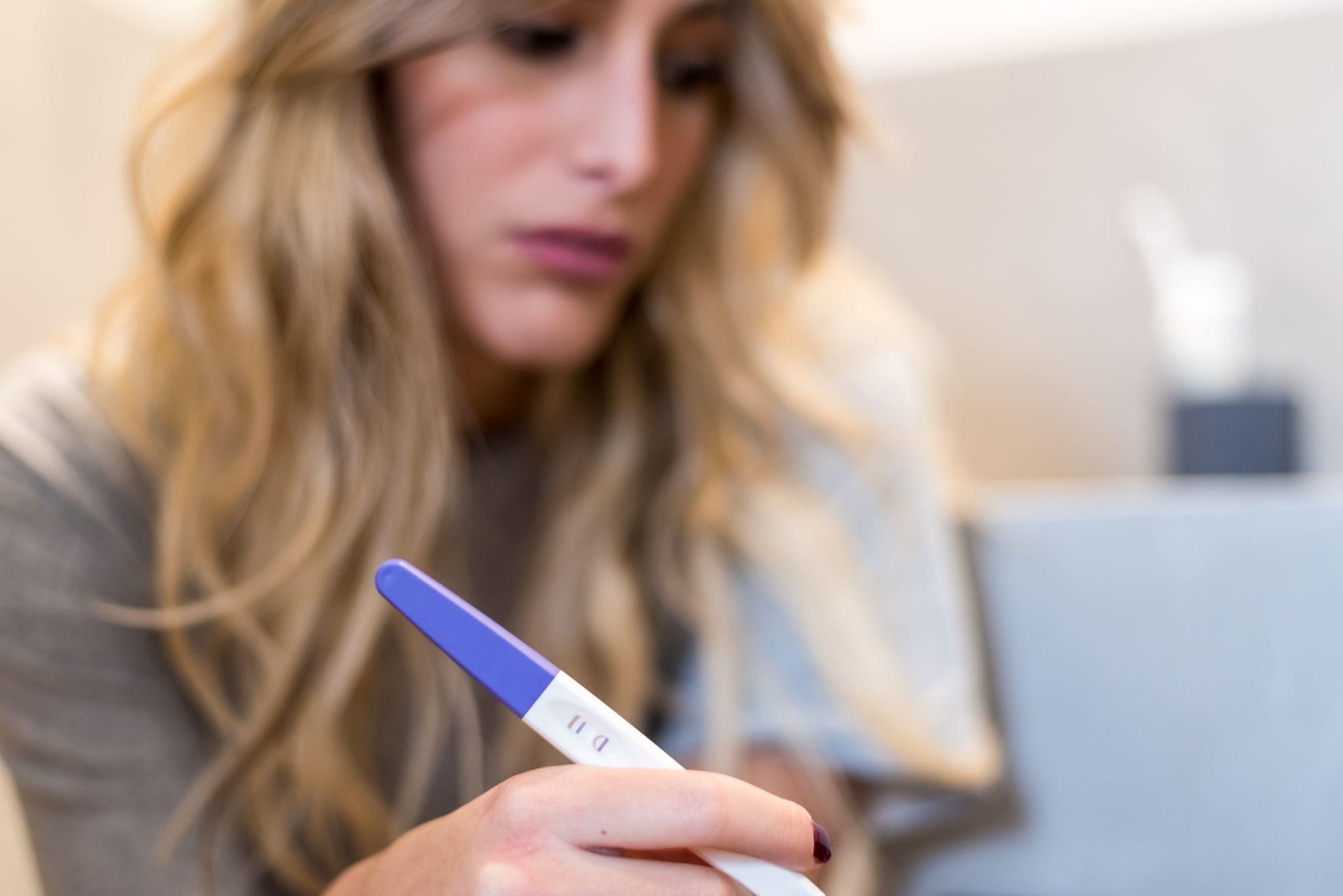 A woman holding a pregnancy test with a positive result beside antenatal vitamins and a glass of water.