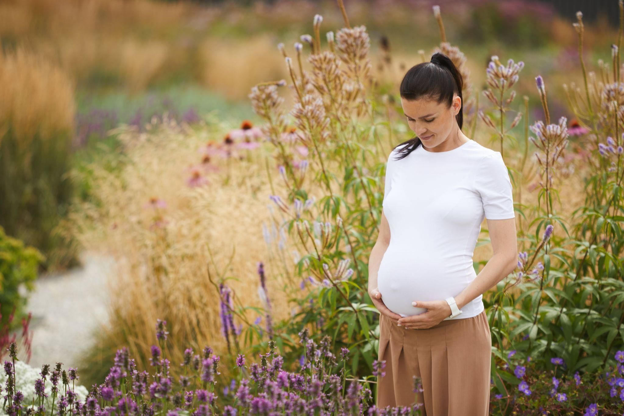 An expectant mother outdoors in a green park with London’s skyline in the background.