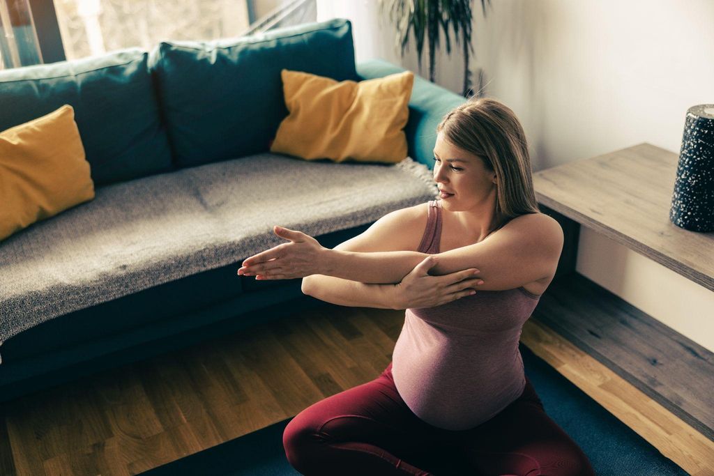 A pregnant woman in her third trimester performs gentle yoga poses at home.