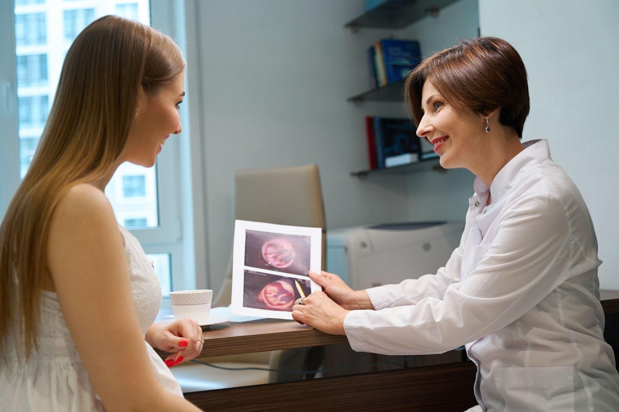 Obstetrician discusses pregnancy health and ultrasound images with pregnant woman during antenatal appointment.