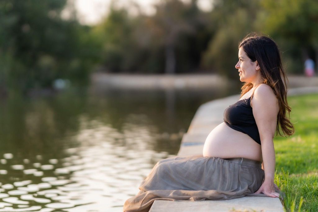 Pregnant woman sits relaxing on riverbank with feet in water. Antenatal anxiety coping measure.