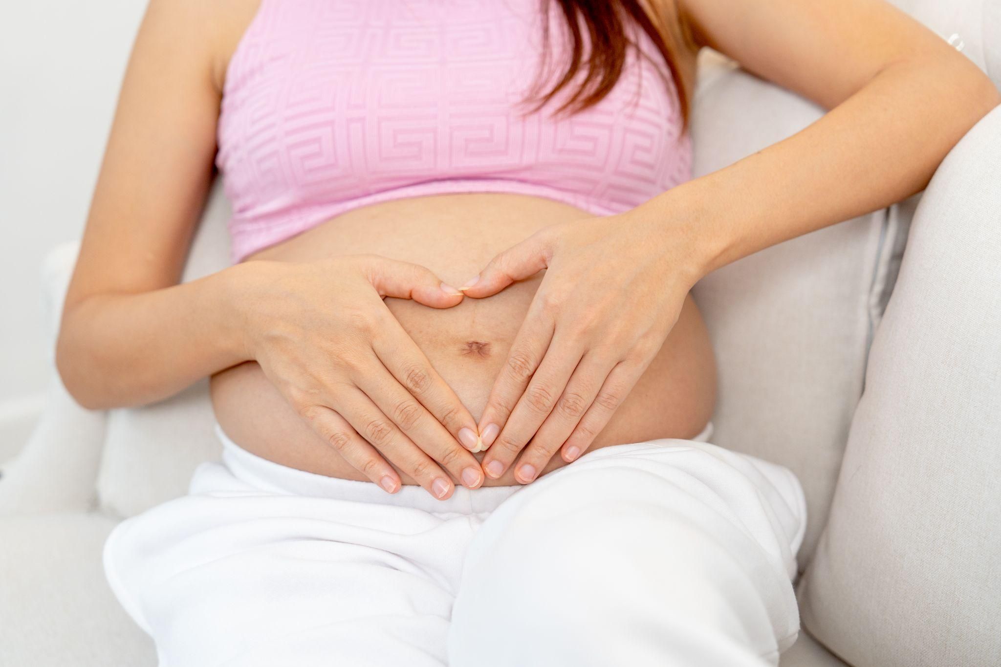 Pregnant woman sits with hands on baby bump.