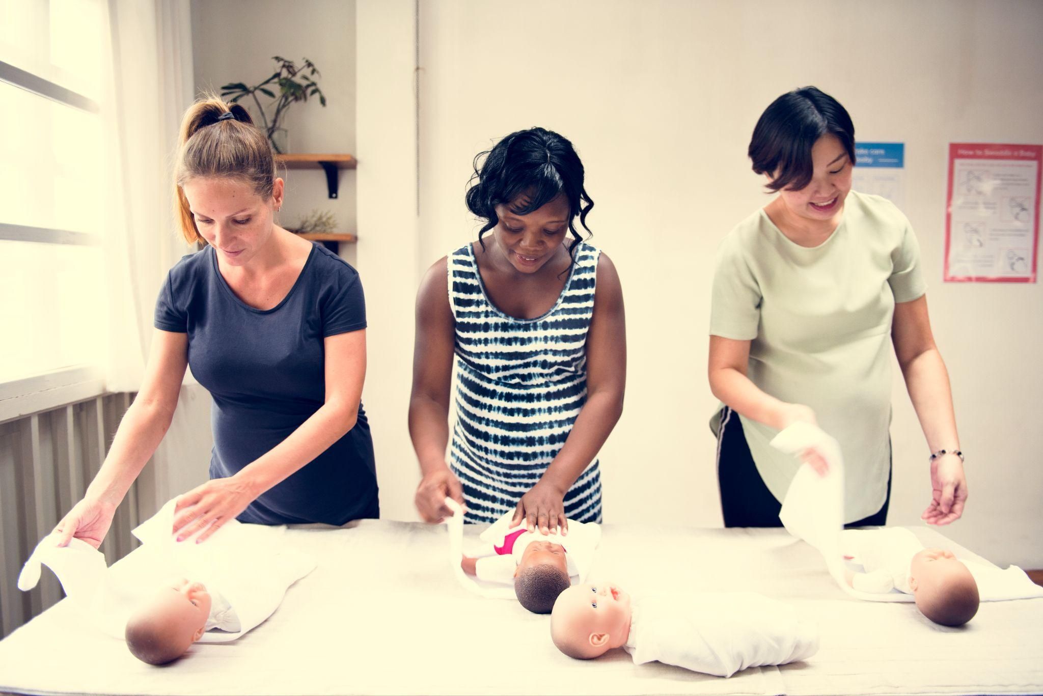 A midwife showing new parents how to swaddle a baby in a postnatal class.