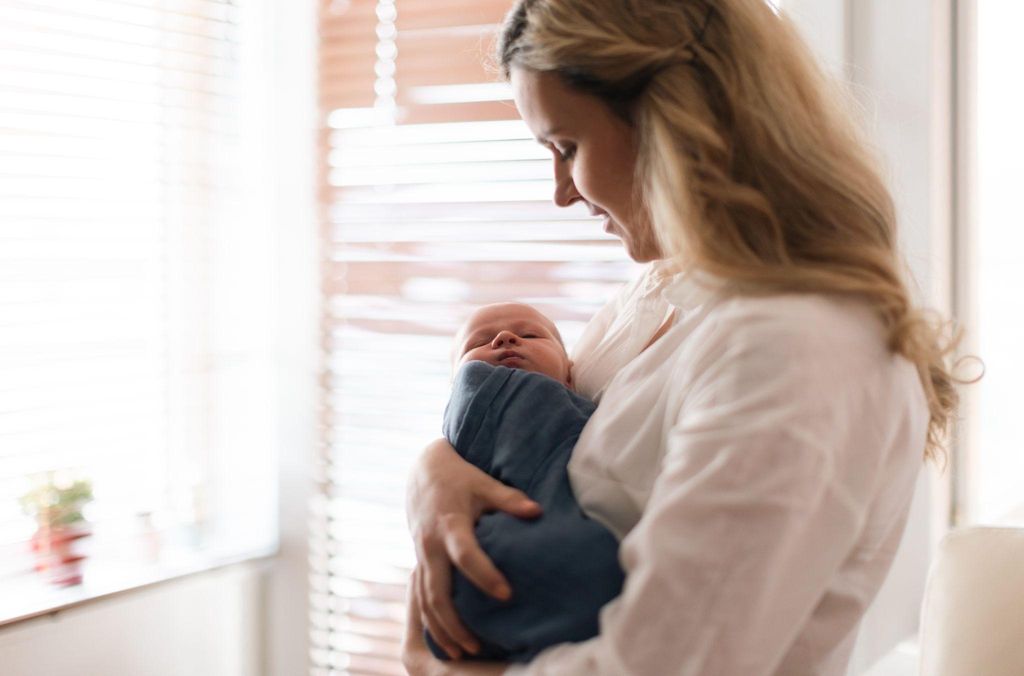 A parent sitting in a quiet room, holding a sleeping newborn in their arms.