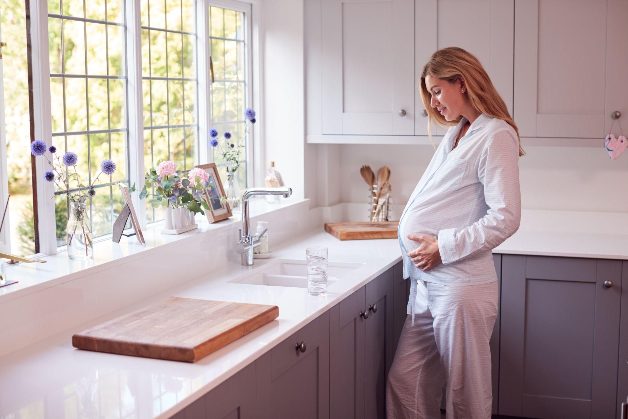 Pregnant woman smiling while showcasing her baby bump in elegant pyjamas.