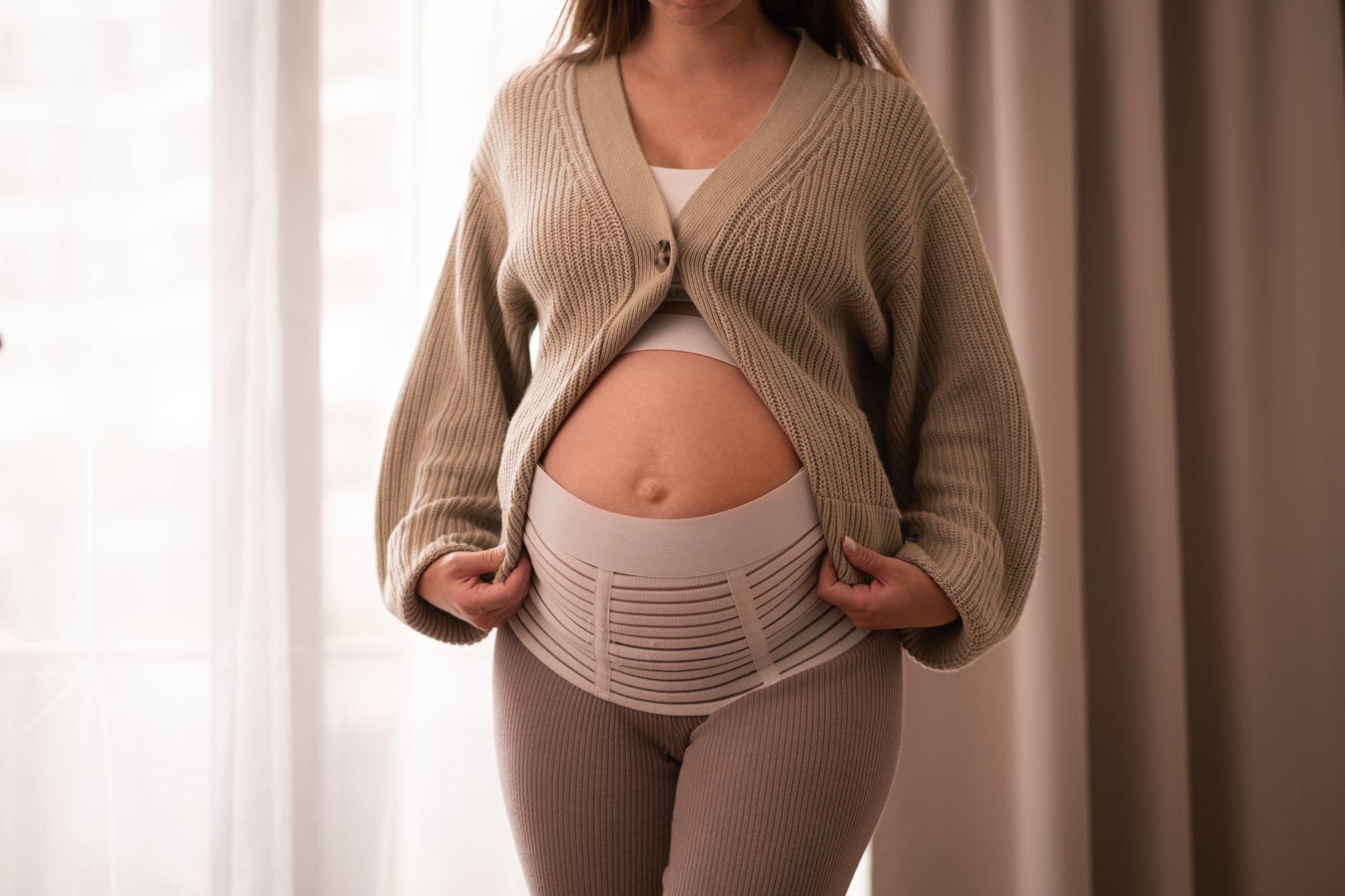 Pregnant woman using a belly band to extend her trousers during pregnancy.