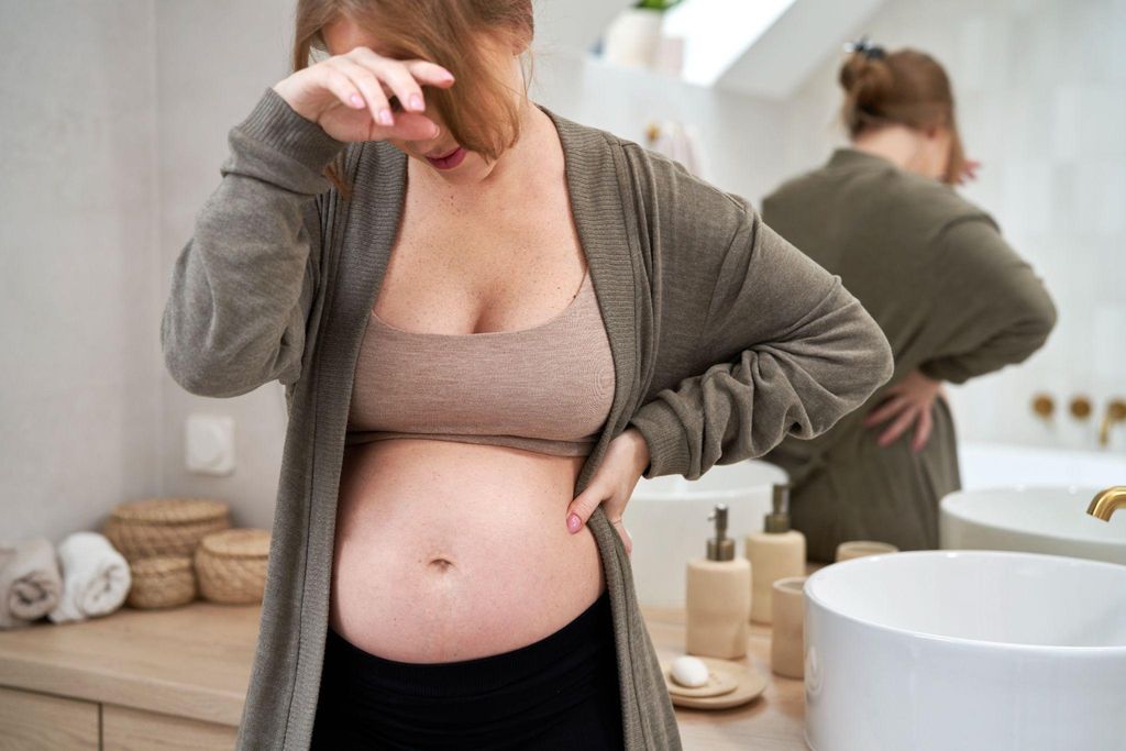 Mum holding a baby carrier while pregnant and smiling.