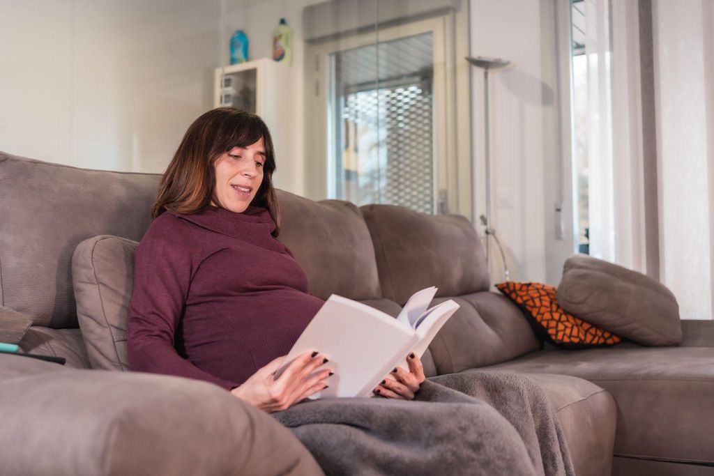 "Pregnant woman reading a book in a relaxing environment."