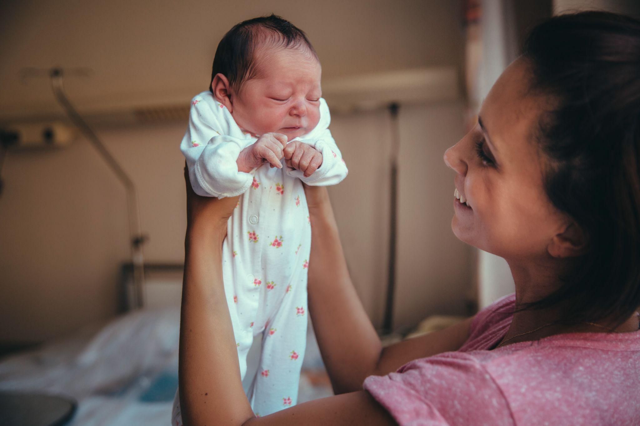 Happy mother admires newborn baby after birth in hospital.