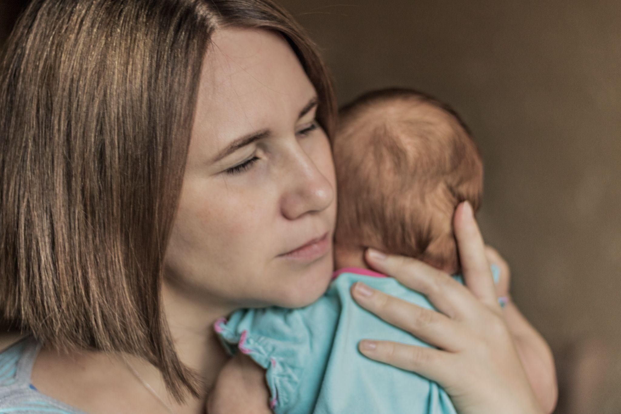 A new mother feeling emotionally overwhelmed while holding her newborn baby.