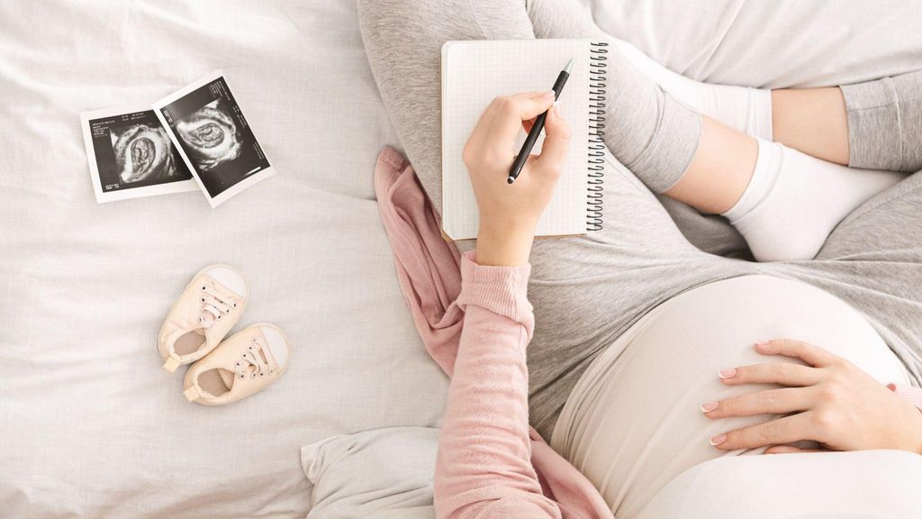 A pregnant woman writing down her birth preferences in a notebook while discussing options with her healthcare provider during an antenatal appointment.