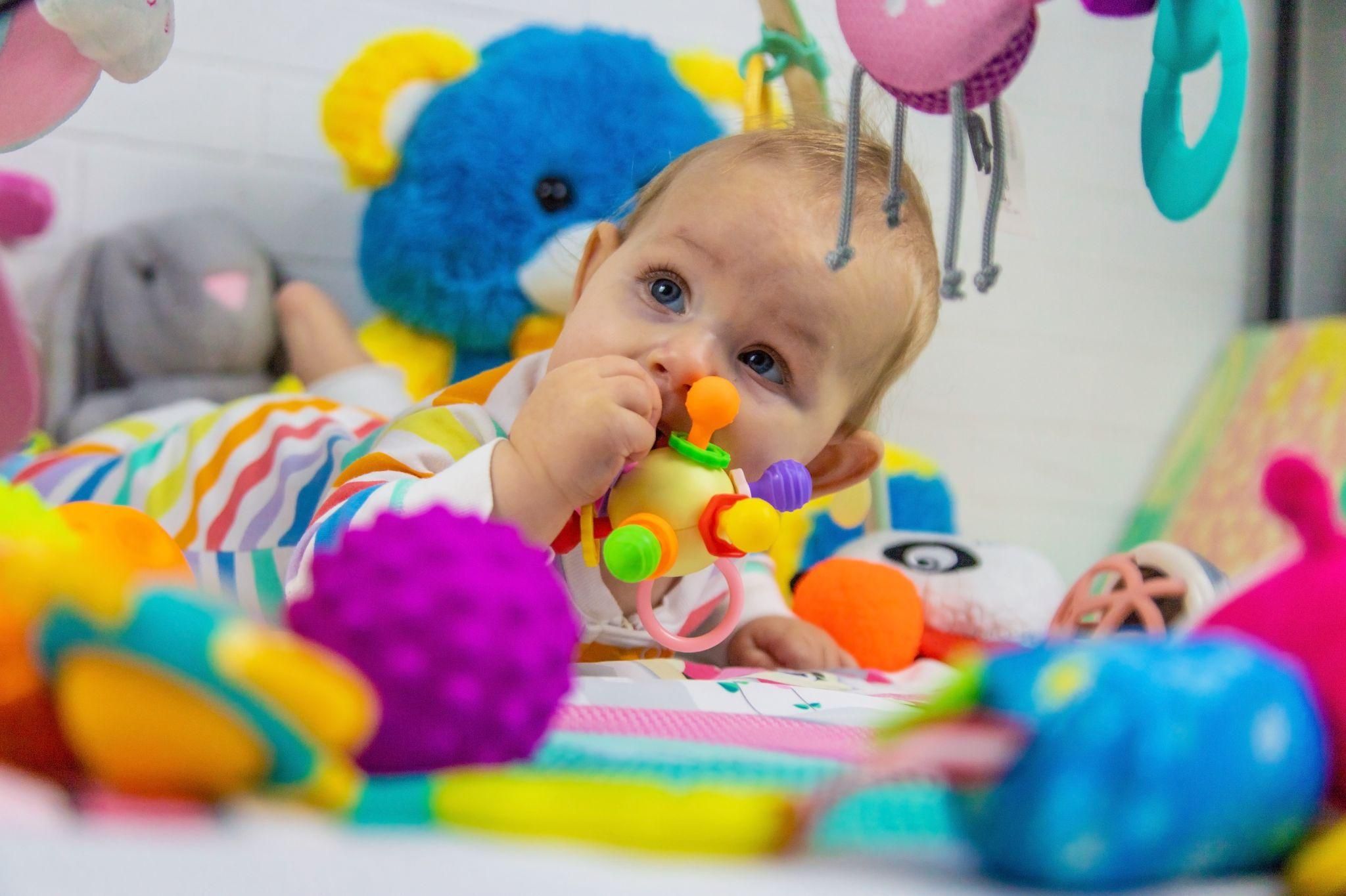 A baby playing with brightly coloured sensory and motor skill development toys.