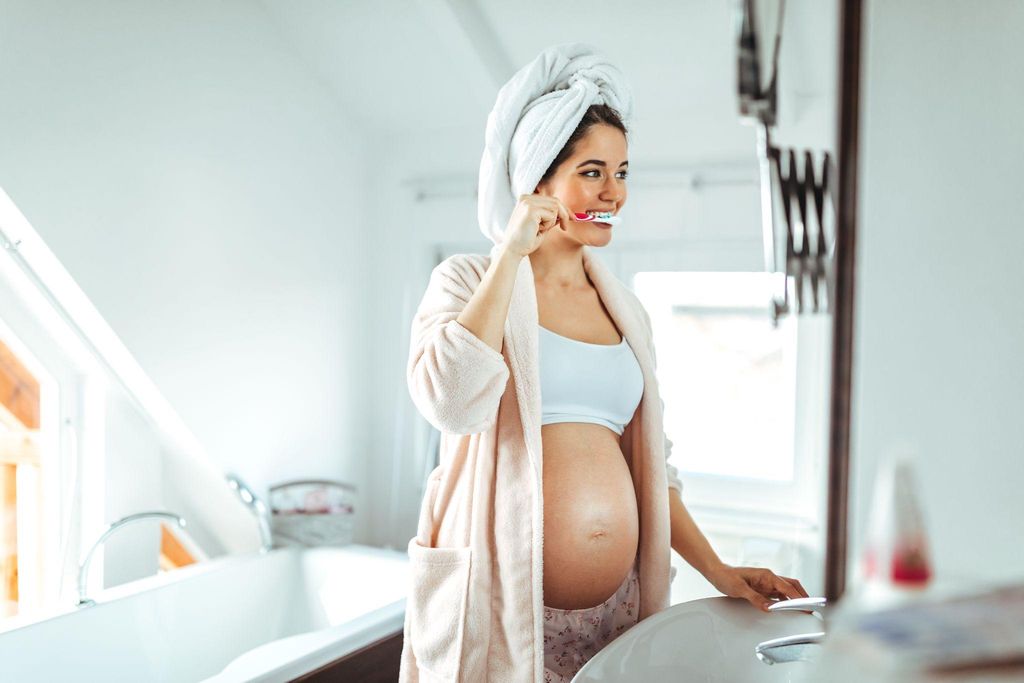 A pregnant woman smiling while brushing her teeth in the morning.