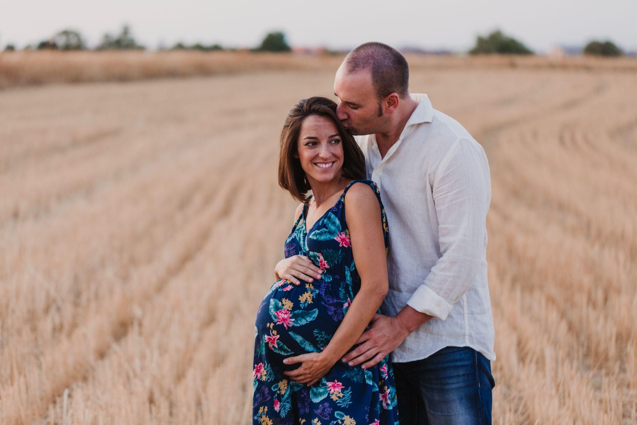 Pregnant woman in a meadow, posing in a flowy dress during golden hour.