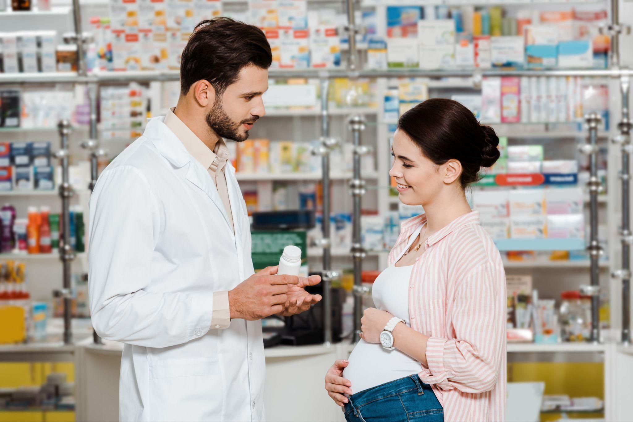 Pharmacist speaks to pregnant woman about medication in chemist.